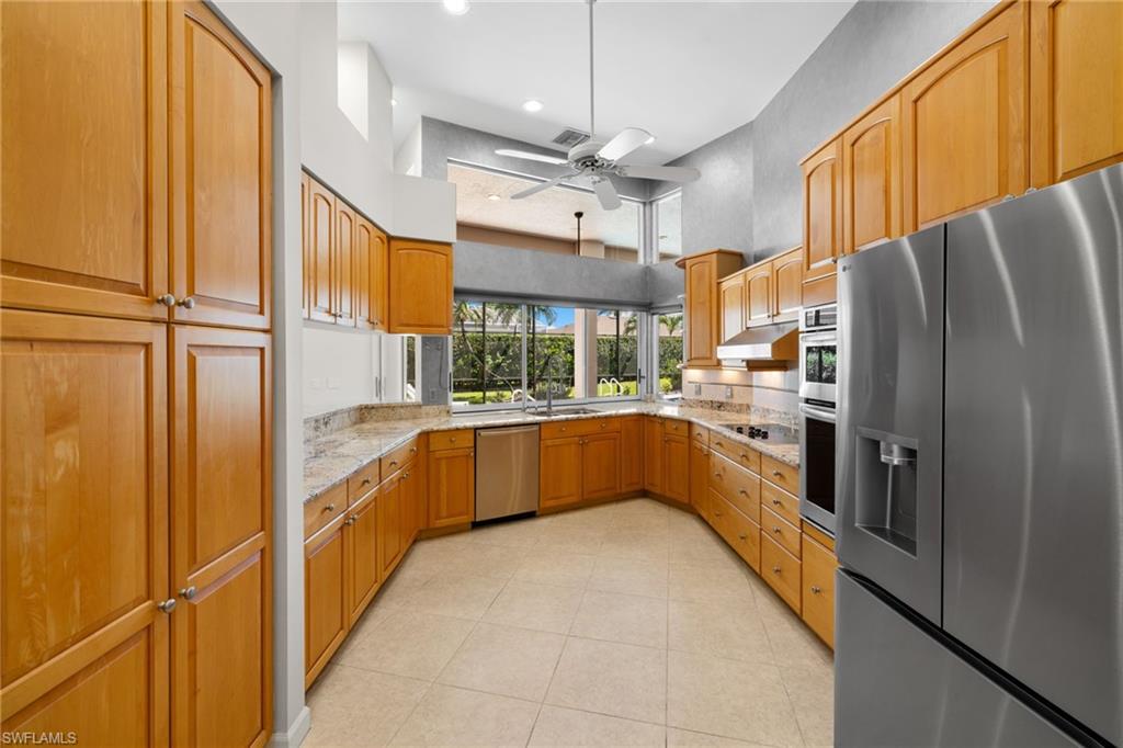 Spacious kitchen featuring light wood cabinetry, stone-finish countertops, stainless steel appliances, and a ceiling fan