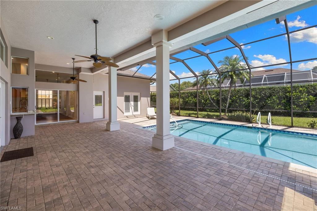 Screened-in outdoor living space featuring an in-ground swimming pool, brick paver patio, and multiple ceiling fans