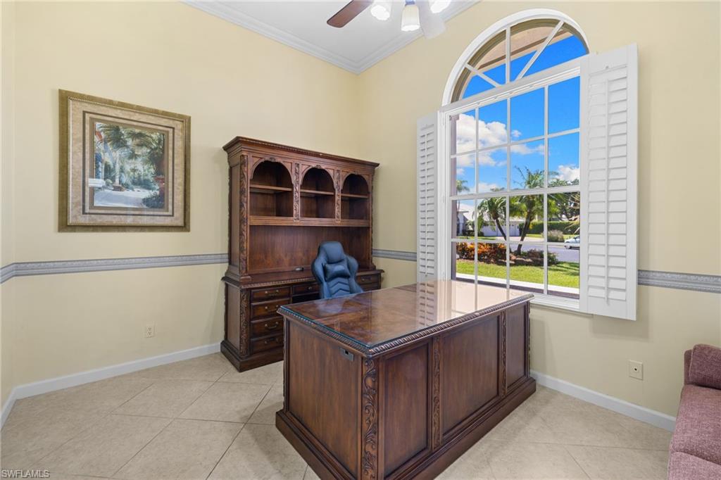 Den/office featuring a large arched window with white plantation shutters, vaulted ceiling, crown molding, and tiled flooring