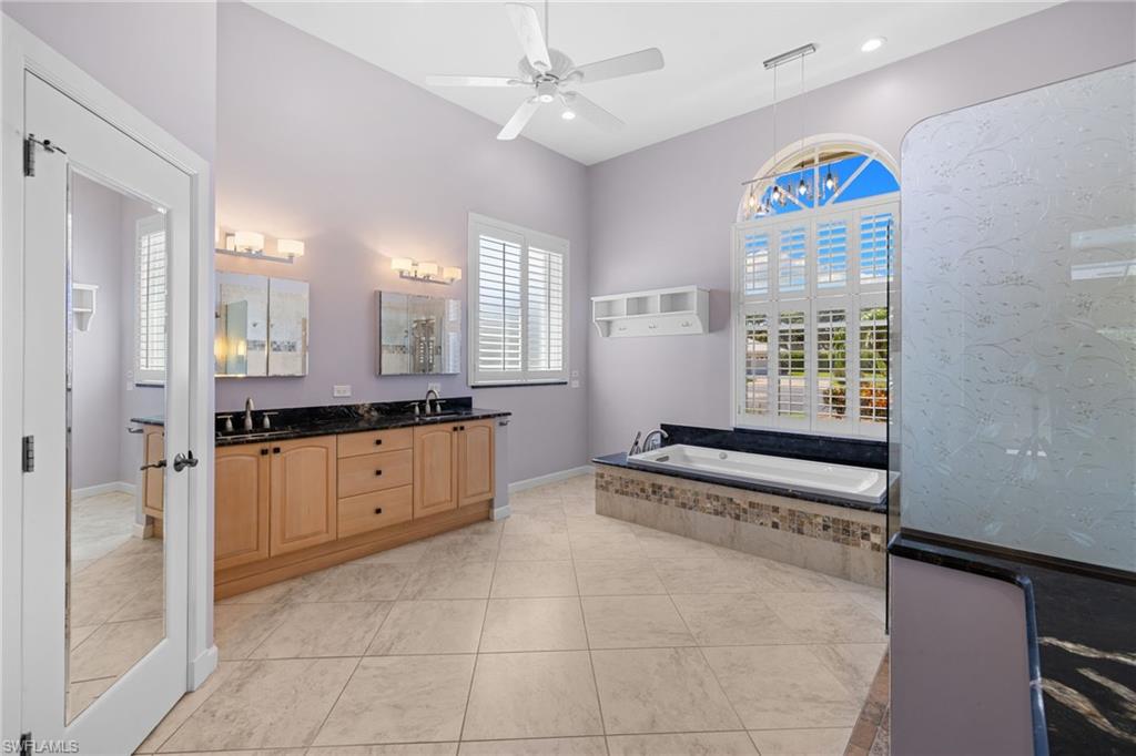 Primary bathroom #1 featuring an integrated soaking tub with stone surround, a dual vanity with a granite countertop, and tiled flooring