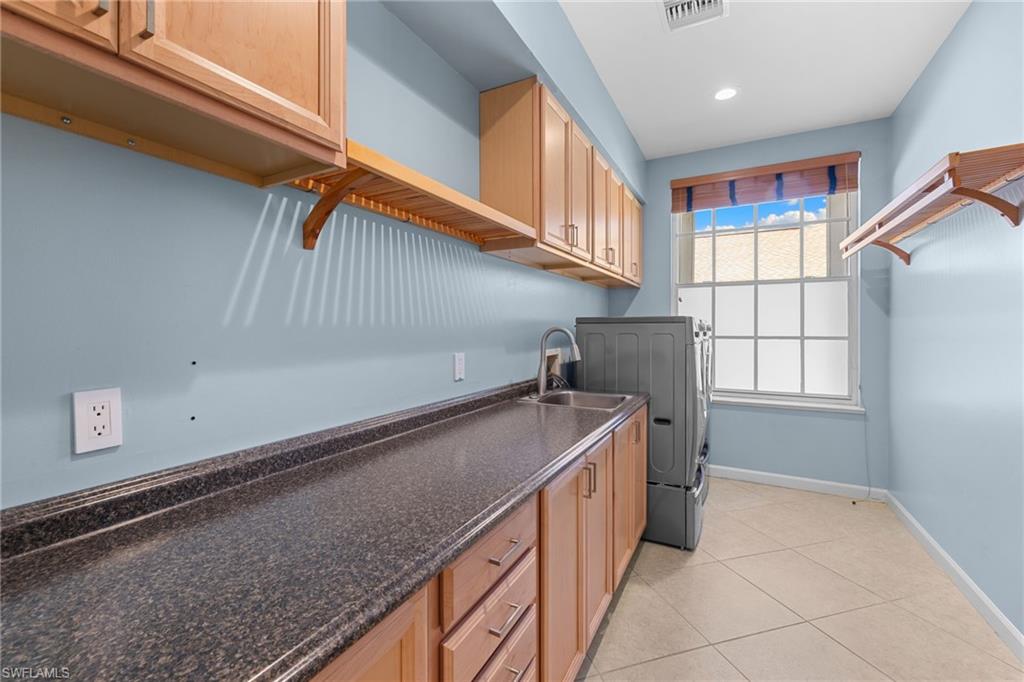 Dedicated laundry room featuring abundant cabinetry, a built-in sink with a gooseneck faucet, durable stone-finish countertops, and tiled flooring