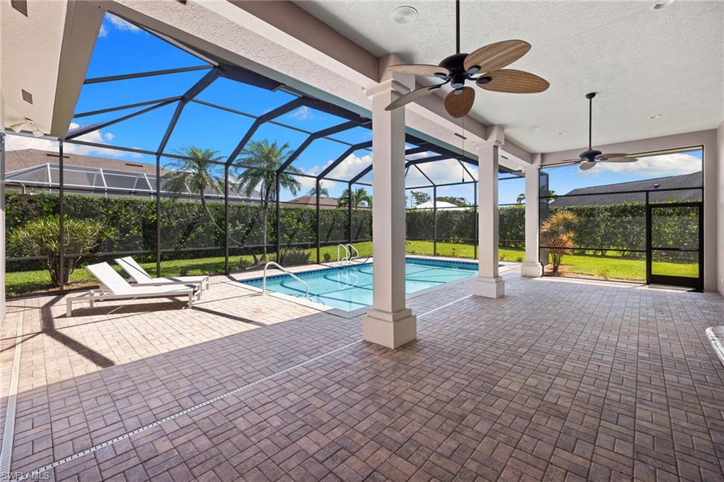 Expansive screened lanai featuring a paver patio, a rectangular swimming pool, multiple ceiling fans, and structural columns