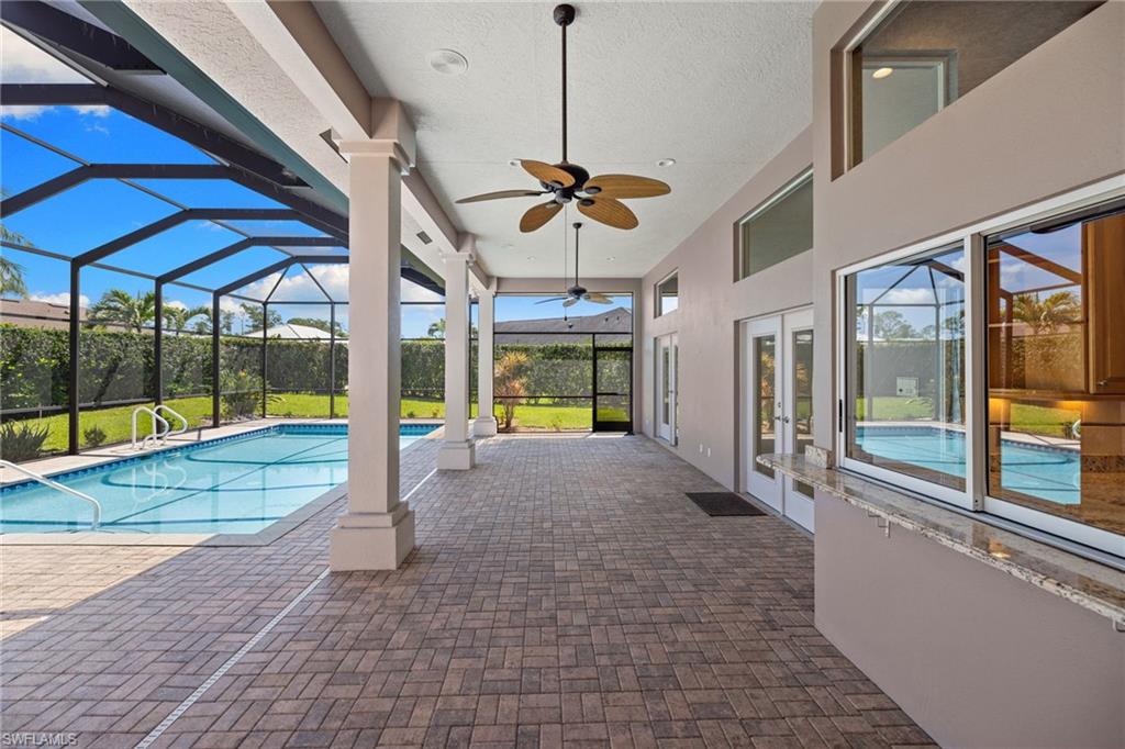 Expansive screened lanai featuring a swimming pool, paver flooring, multiple ceiling fans, and a pass-through serving window with a stone countertop
