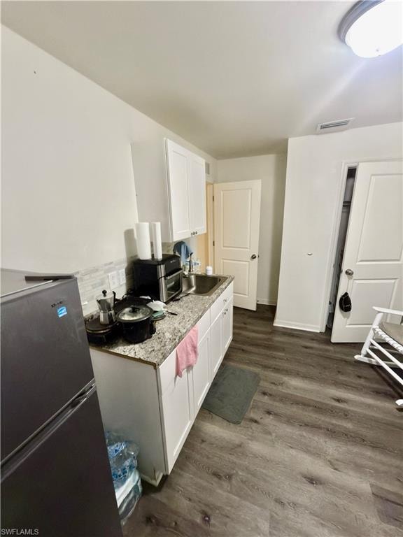Compact kitchen area featuring white upper and lower cabinetry, a stone-finish countertop, and a stainless steel sink with a tile backsplash