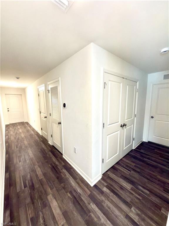 Hallway featuring wood-finish flooring, white baseboards, white walls, and multiple white panel doors