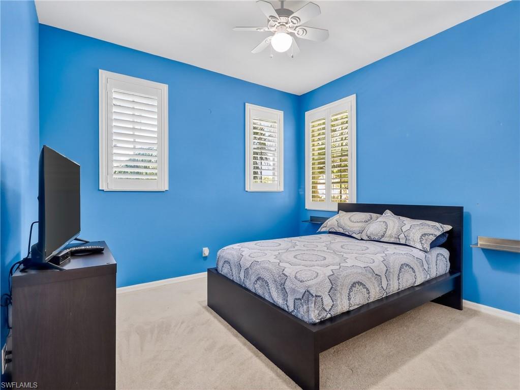 Bedroom with light carpet, a ceiling fan, and multiple windows