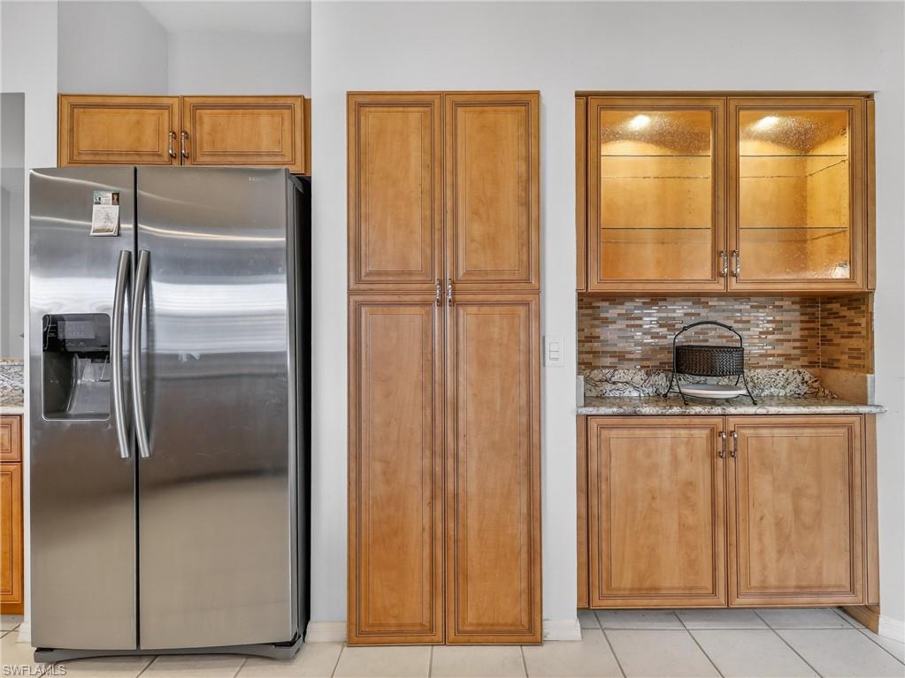Kitchen with stainless steel fridge, tasteful backsplash, light granite countertops, and wood finish cabinetry
