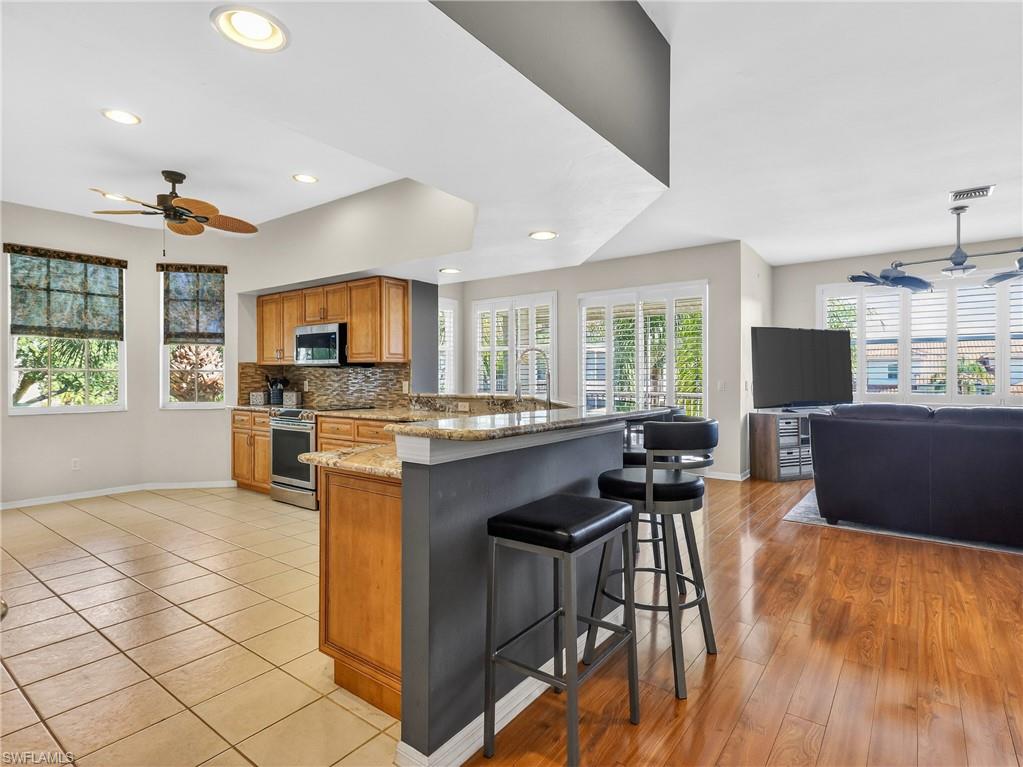 Kitchen featuring ceiling fan, stainless steel appliances, open floor plan, wood finish cabinets, and light stone countertops