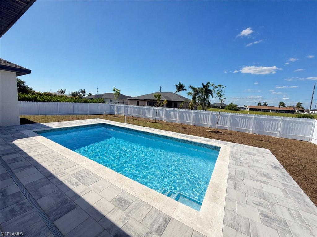 Backyard featuring an in-ground swimming pool with steps, surrounded by light-toned paver decking