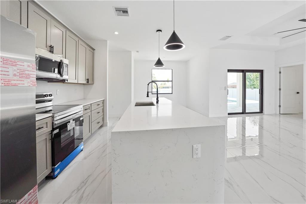 Kitchen featuring light gray cabinetry, stainless steel appliances, and a white countertop with an integrated sink and matte black faucet
