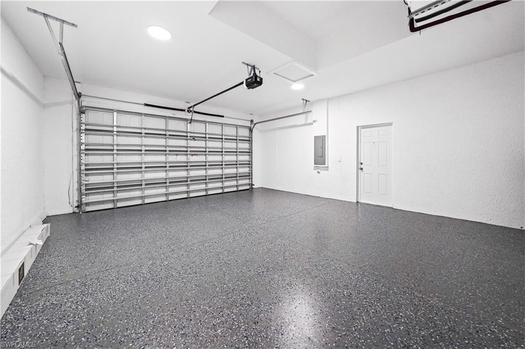 Spacious garage featuring a durable speckled epoxy floor, overhead lighting, an automatic garage door opener, and a side entry door