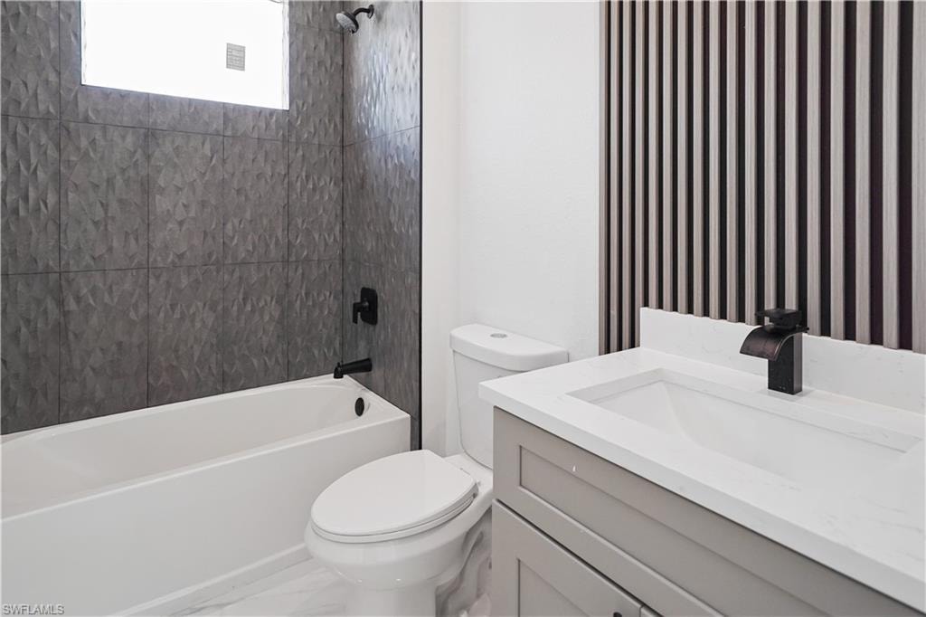 Bathroom featuring a textured gray tile shower surround, a white bathtub, and a modern vanity with an integrated sink and dark bronze faucet