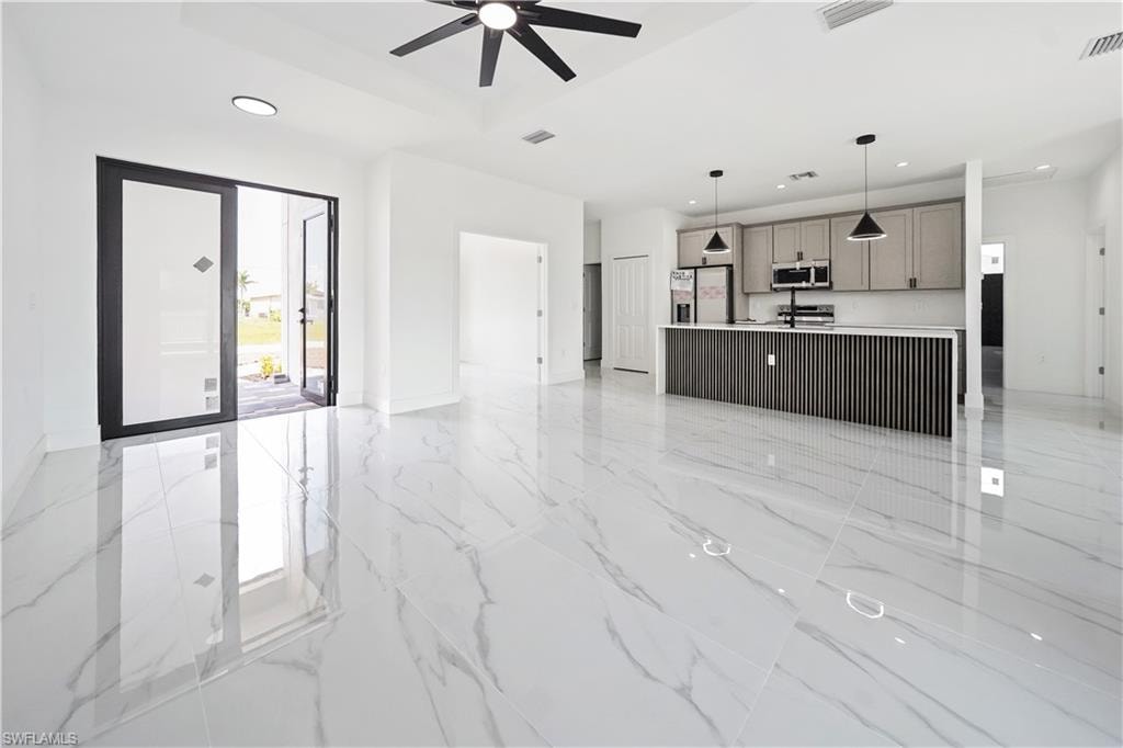 Spacious open-concept living area featuring large format white tile flooring, contemporary kitchen island with ribbed detailing, recessed lighting, modern ceiling fan, and double entry doors with frosted glass panels