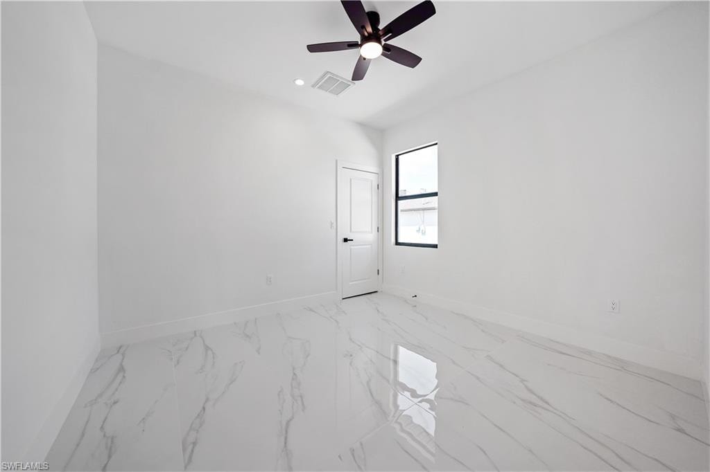Spacious room featuring white walls, high ceilings, a contemporary ceiling fan, and large format marble-look flooring