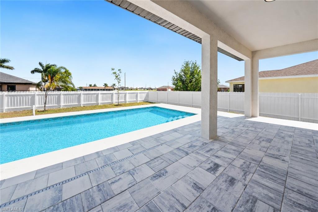 Expansive outdoor living area featuring a covered patio with tile flooring, a rectangular swimming pool, and a white privacy fence