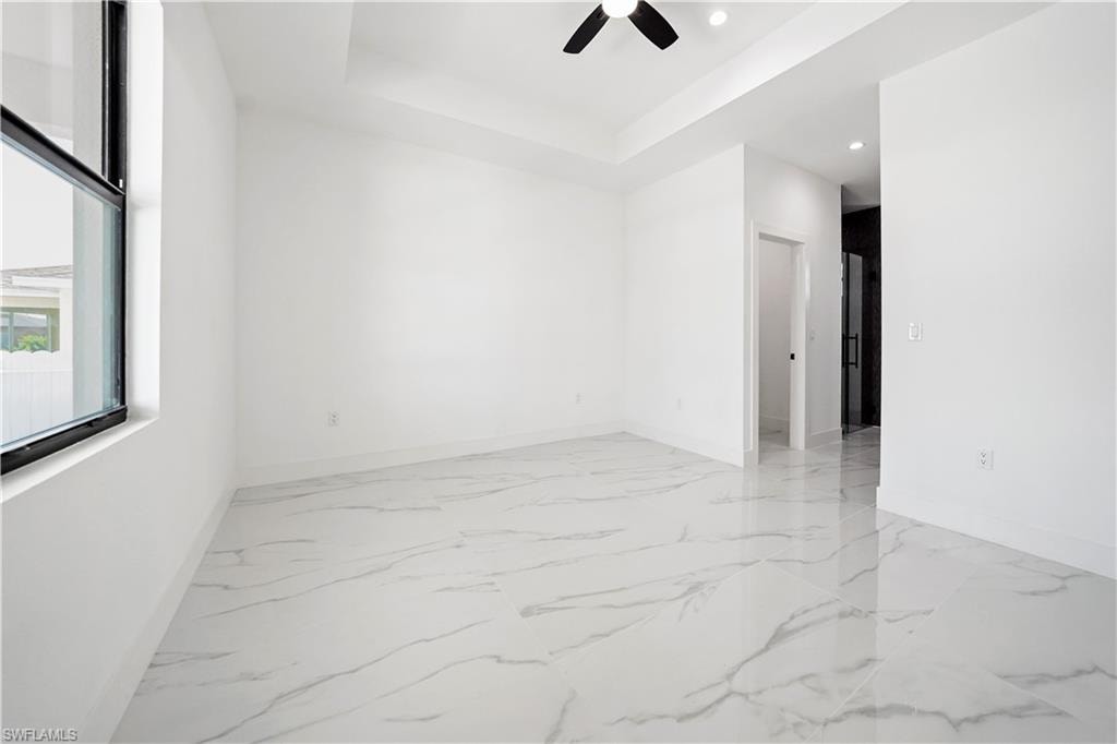 Spacious room featuring large format tile flooring, a tray ceiling, recessed lighting, and a ceiling fan