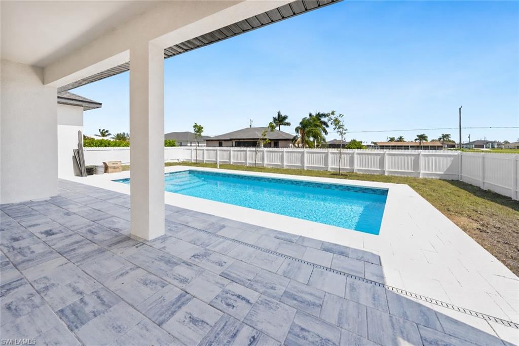 Expansive outdoor living area featuring a rectangular swimming pool, concrete paver patio, and a privacy fence