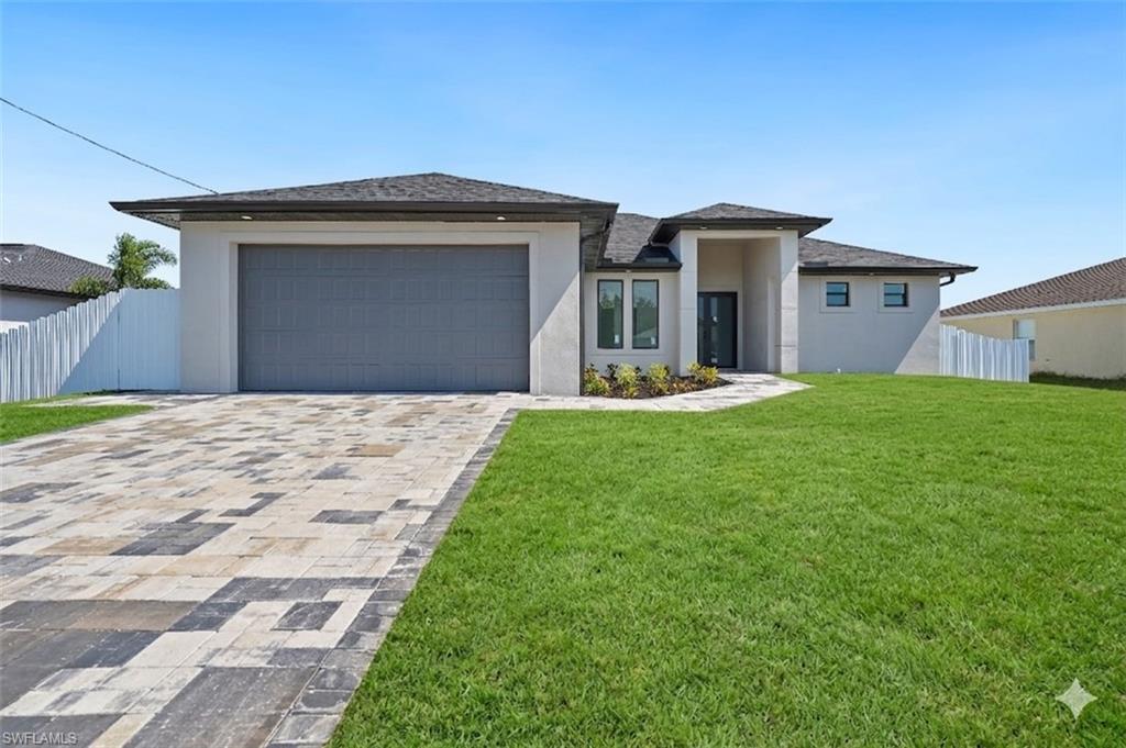 Contemporary stucco exterior with a gray panel garage door, a patterned paver driveway, a covered entry, and a manicured lawn