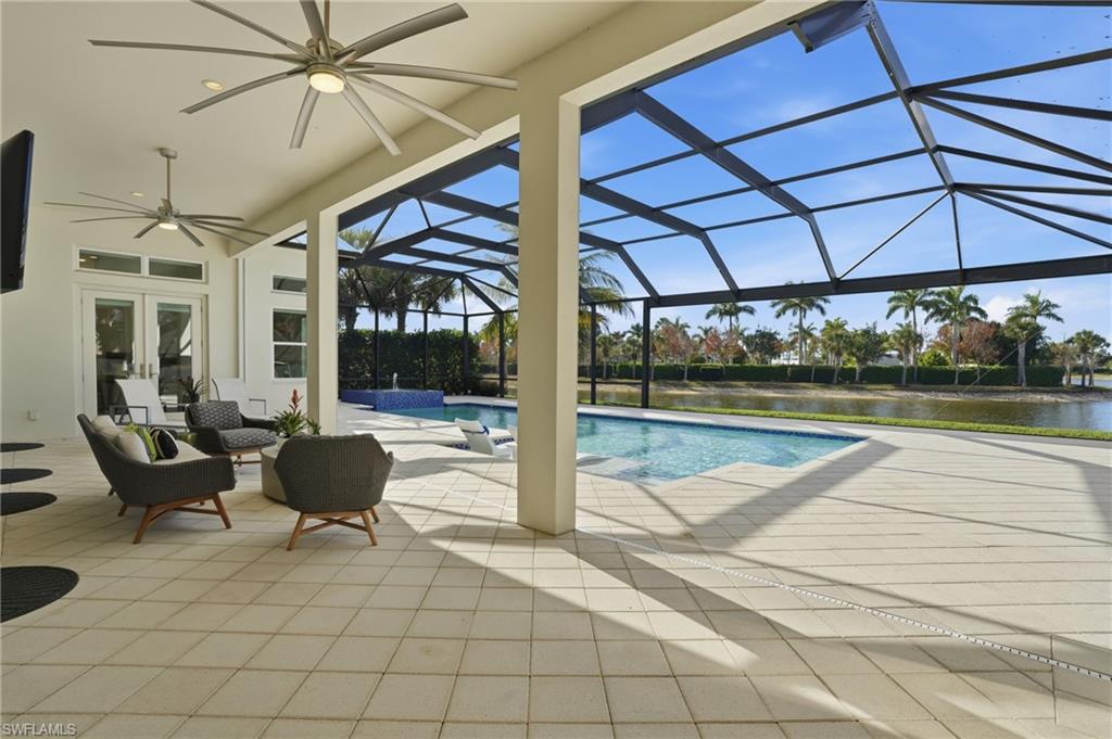 Spacious covered lanai featuring large format tile flooring, multiple ceiling fans, and direct access to the screened pool area with a water feature, all overlooking a serene waterway