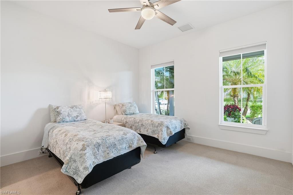 Bedroom with two windows offering tropical foliage scenery, neutral carpeting, and a ceiling fan with integrated lighting