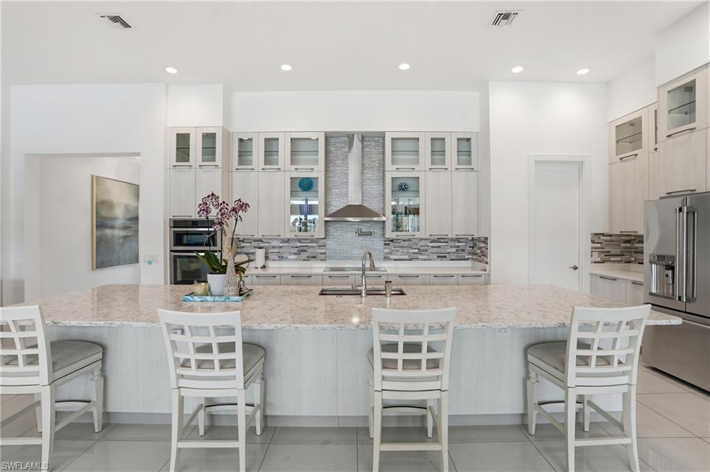 Spacious kitchen featuring a large island with seating, stainless steel appliances, extensive cabinetry, and a decorative tile backsplash