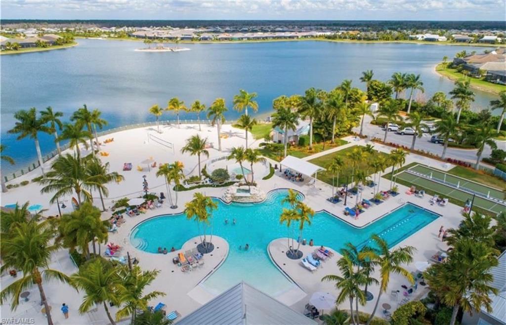 Expansive aquatic amenity featuring a large freeform pool, a dedicated lap pool, and a white sand beach area with mature palm trees