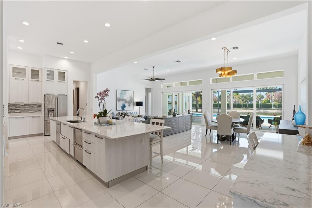 Gourmet kitchen featuring a large island with sink, white shaker cabinetry, stainless steel appliances, and a mosaic tile backsplash