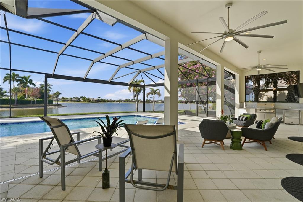 Expansive screened lanai featuring a built-in pool, a lake backdrop, tile flooring, an outdoor kitchen with a built-in grill, and multiple ceiling fans