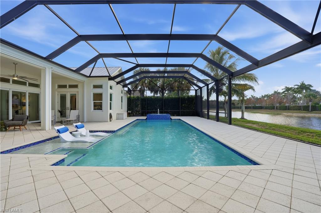 Screened pool area featuring a rectangular swimming pool with integrated spa and water feature, light-toned paver decking, and a tranquil water body beyond