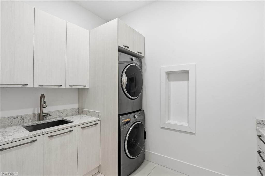 Laundry area featuring stacked front-load machines, light wood-finish cabinetry, a deep basin sink with a gooseneck faucet, and light-toned countertop