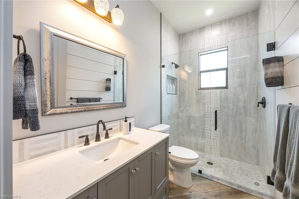 Bathroom featuring a glass-enclosed shower with a window, a single-sink vanity with a light countertop and dark cabinetry, a framed mirror, and wood-finish flooring