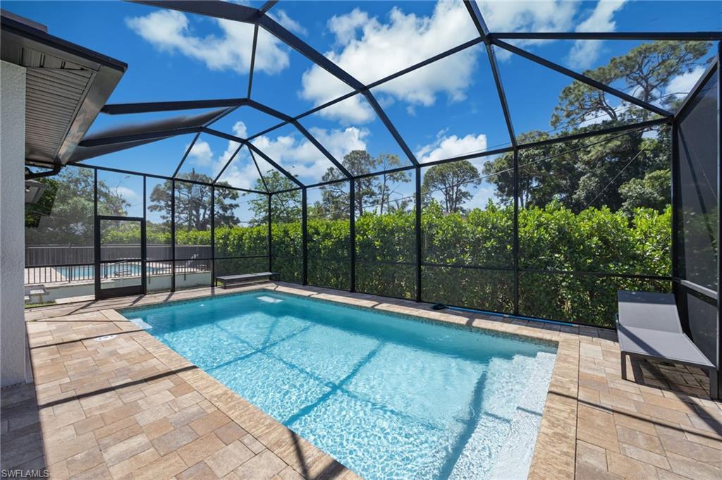 Screened outdoor living area featuring a rectangular pool with integrated steps, paver decking, and mature landscaping