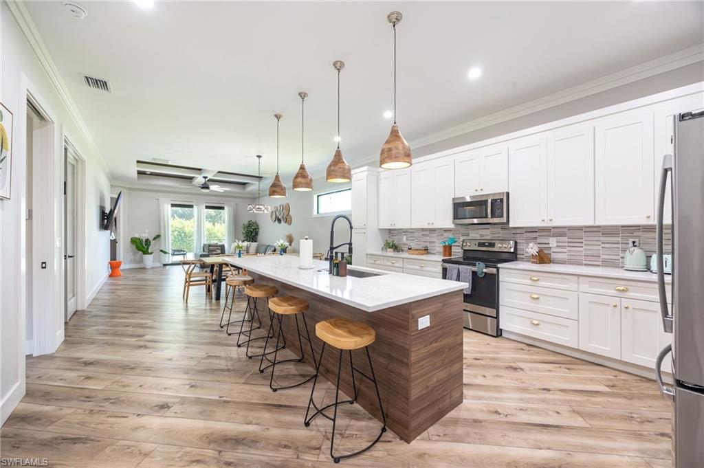 Open-concept kitchen featuring an expansive island with seating, white cabinetry, a tiled backsplash, and stainless steel appliances