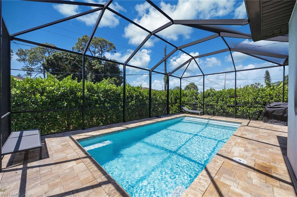 Screened-in pool area featuring a rectangular swimming pool, paver decking, and mature perimeter landscaping