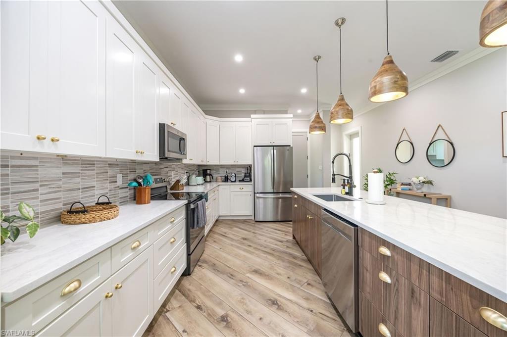 Modern kitchen featuring white shaker cabinetry with gold-toned hardware, light-toned countertop surfaces, and a linear tile backsplash