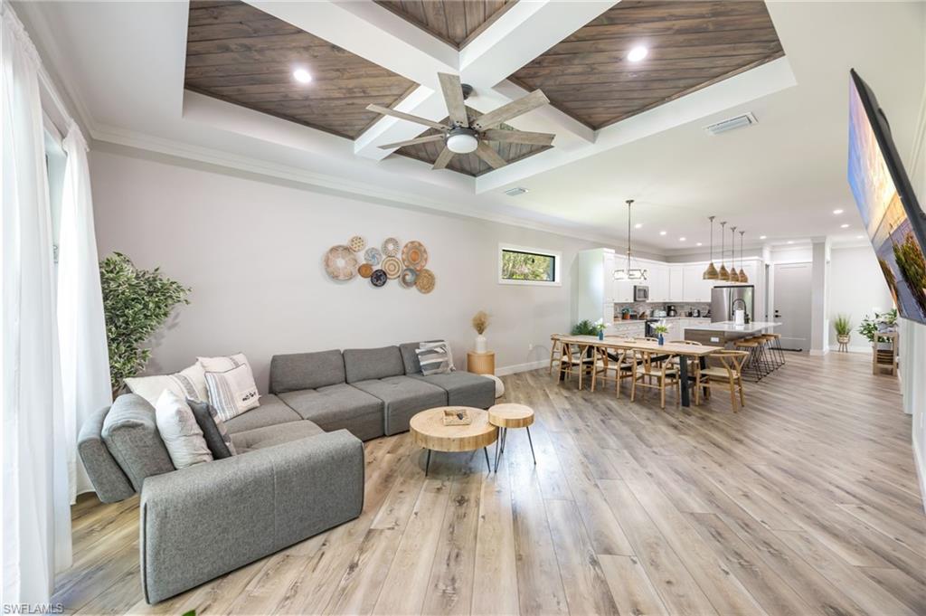Expansive living area with wood-finish flooring, a coffered ceiling with wood-paneled inserts, and recessed lighting