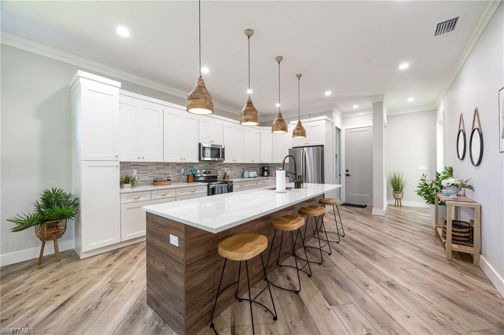 Modern kitchen featuring a large island with a white countertop and wood-finish paneling, pendant lighting, white cabinetry, stainless steel appliances, and wood-finish flooring