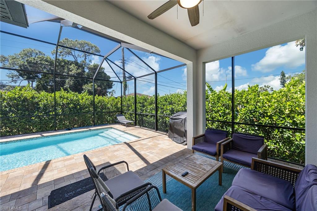 Screened outdoor living area featuring a rectangular pool, paver deck, and mature privacy hedging