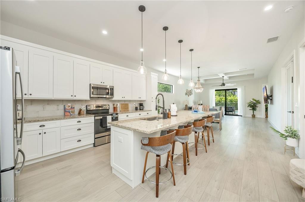 Expansive kitchen featuring white cabinetry, stainless steel appliances, granite countertops, and a large island with pendant lighting