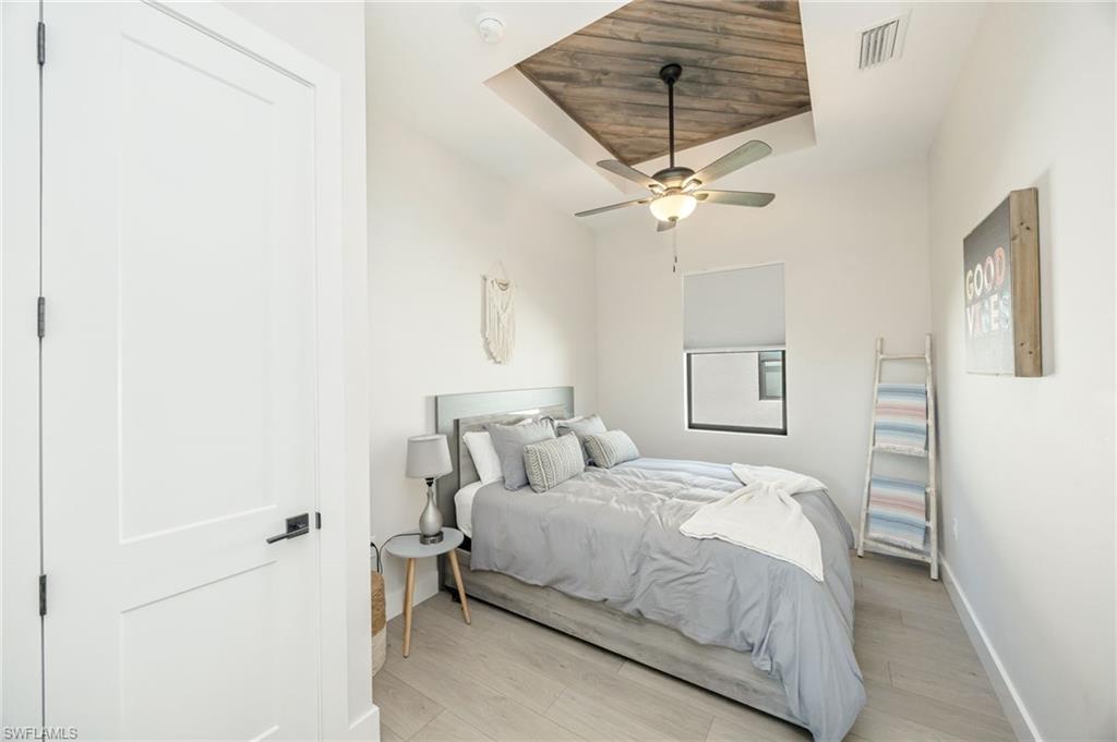 Recessed ceiling with wood-finish paneling, ceiling fan with integrated lighting, wood-finish flooring, white flat-panel door with black hardware, and window with roller shade