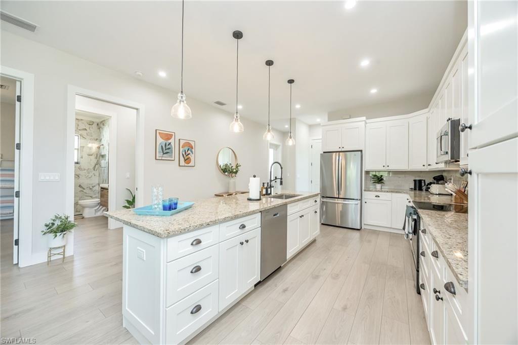 Spacious kitchen featuring white cabinetry, light-toned wood-finish flooring, and a large central island with a granite countertop and pendant lighting