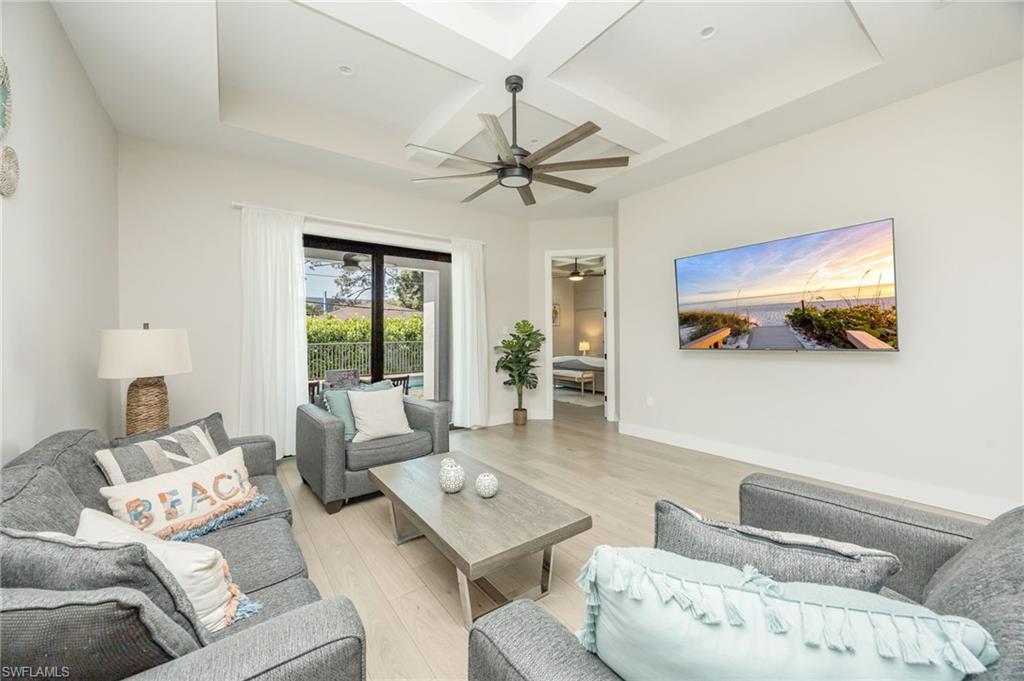 Spacious living area featuring light wood-finish flooring, a tray ceiling with a dark-bladed ceiling fan, and recessed lighting