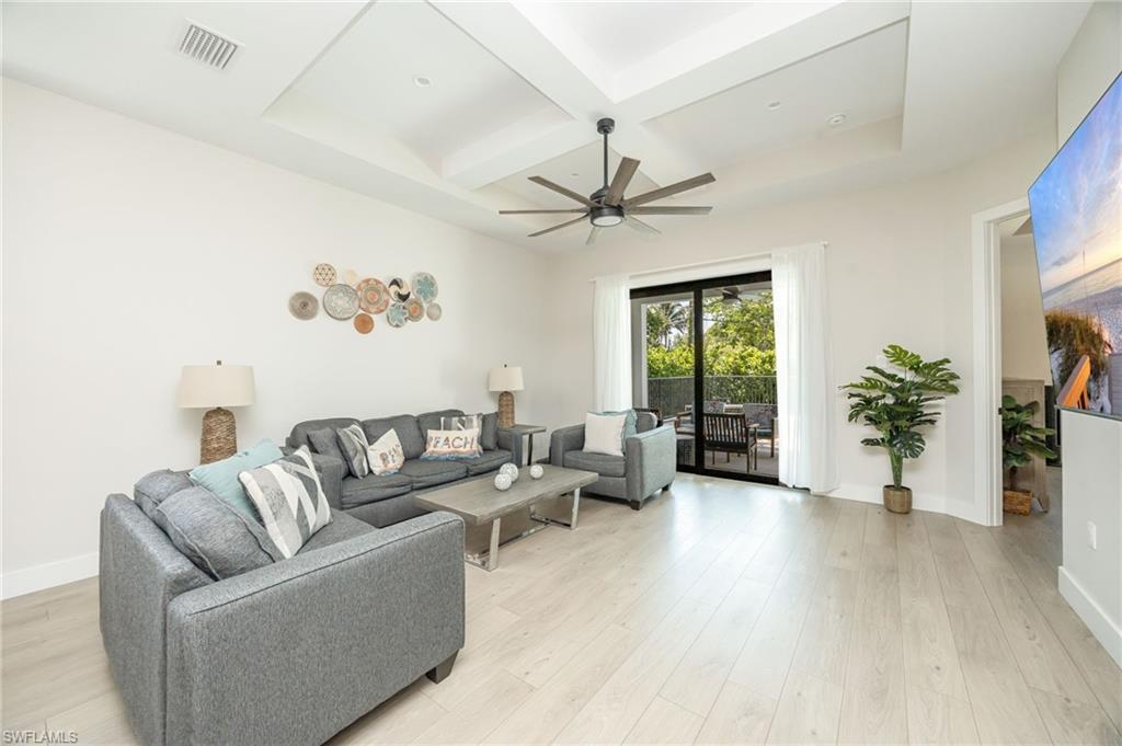 Spacious living area featuring light wood-finish flooring, a tray ceiling with a modern ceiling fan, and sliding glass doors opening to an outdoor patio