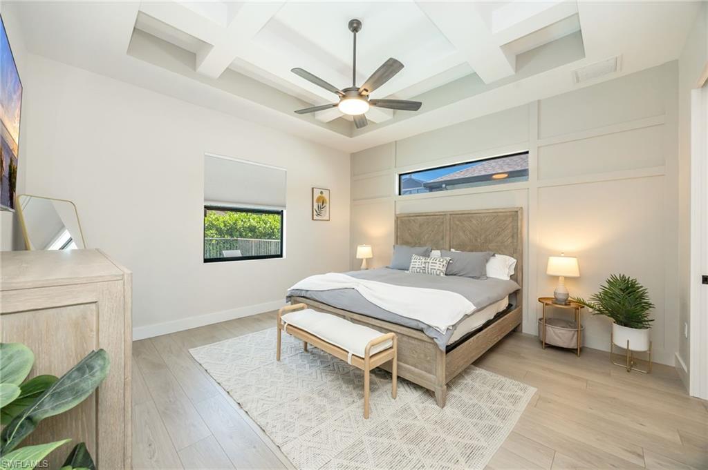 Spacious room featuring a coffered ceiling with a ceiling fan, light wood-finish flooring, and a window with a roller shade