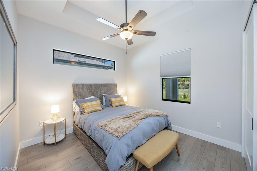 Bedroom featuring light wood-finish flooring, a contemporary ceiling fan with lighting, a tray ceiling, a horizontal transom window, and a roller shade on a standard window