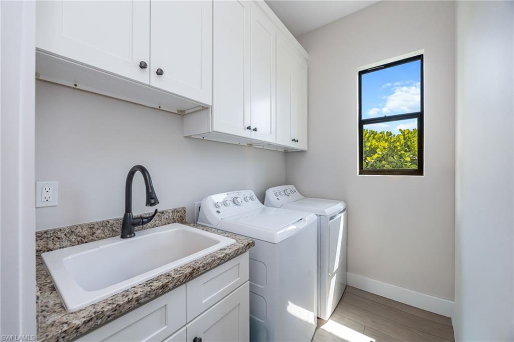 Dedicated laundry space featuring white shaker cabinetry, an undermount utility sink with a matte black faucet, granite-finish countertops, and wood-finish flooring