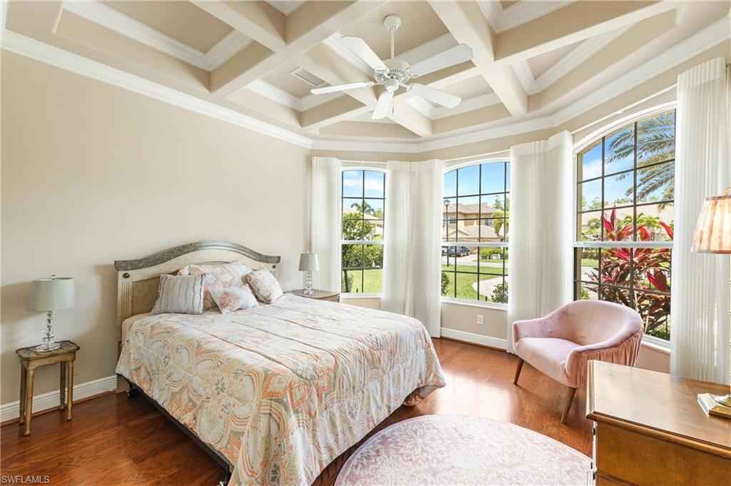 First floor Den being used as a Bedroom featuring hardwood flooring, a coffered ceiling with a ceiling fan, and a curved bay of three windows with arched transoms