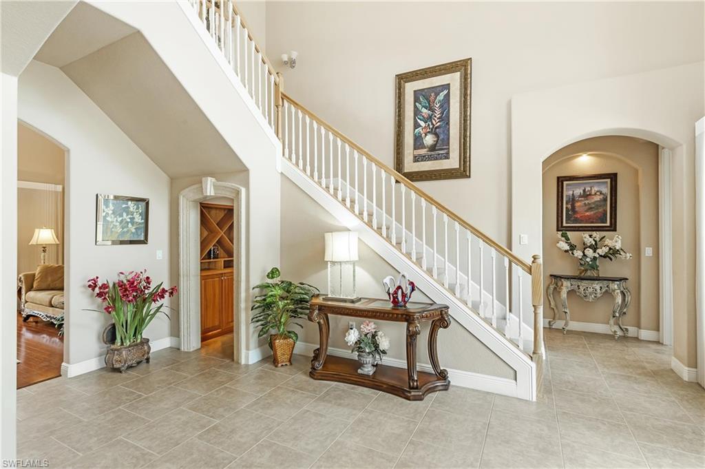 Foyer featuring a grand staircase with white balusters and a wood-finish handrail, tiled flooring, an arched entryway, and a built-in wood-finish cabinet with wine storage