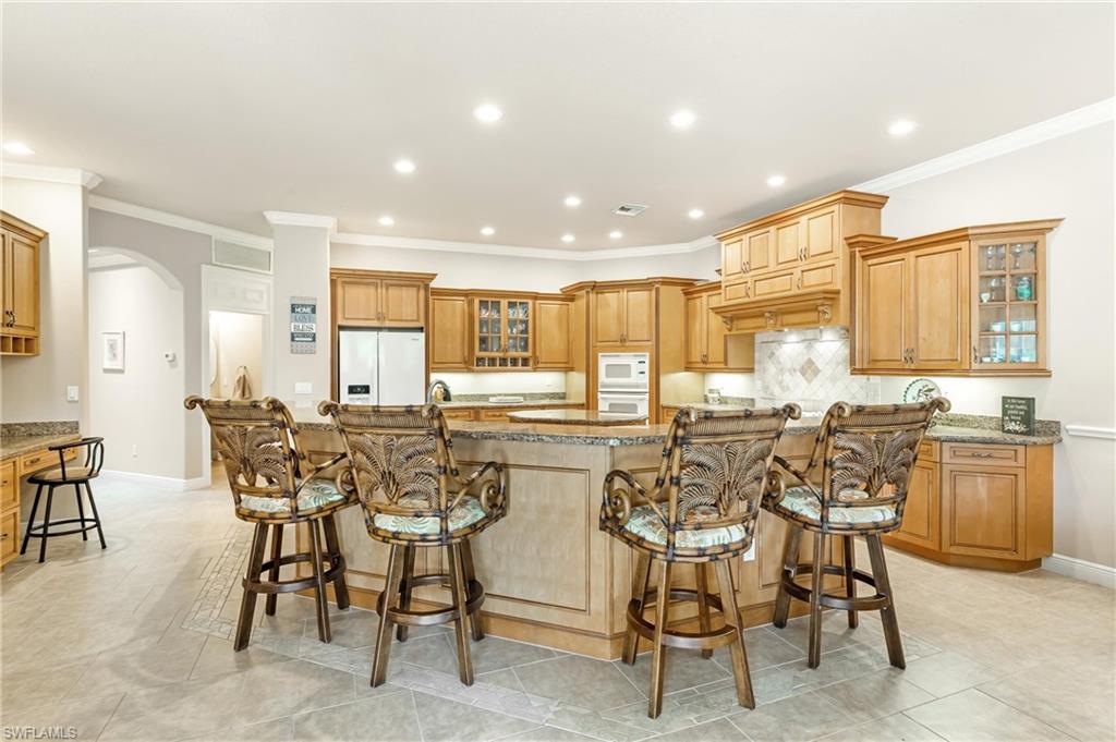 Spacious kitchen featuring breakfast bar, a large central island with seating, extensive wood cabinetry, light-toned countertops, tile backsplash, and recessed lighting