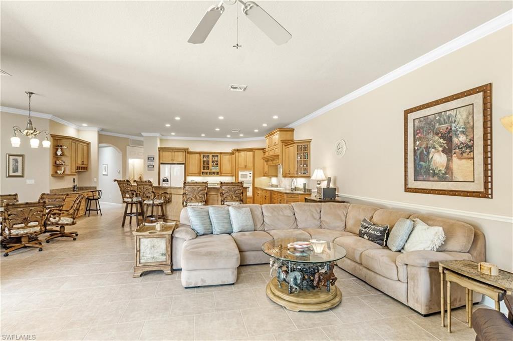 Expansive open-concept living area featuring light-toned tile flooring, recessed lighting, crown molding, and a ceiling fan